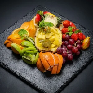 Obst Box von Moment Catering Stuttgart mit saisonalem Obst assortiert: rote Trauben, Apfel, Orange, Ananas, Kiwi, Erdbeeren, Grapefruit, Birne, Physalis – garniert mit Minze und Zitrone, ideal für Business-Events und Kaffeepausen.