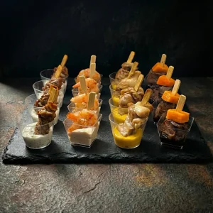 Snack Cups Box von Moment Catering Stuttgart mit 16 Snack-Bechern: Entenfilet mit Nuss-Joghurt-Sauce (Naturjoghurt, Walnüsse, Basilikum), Garnele mit cremigem Räucherlachs-Dip, Chicken mit Kürbis-Curry und Schweinefleisch mit Labneh-Tahini – ideal für Empfang, Stehevent und Business Catering in Stuttgart.